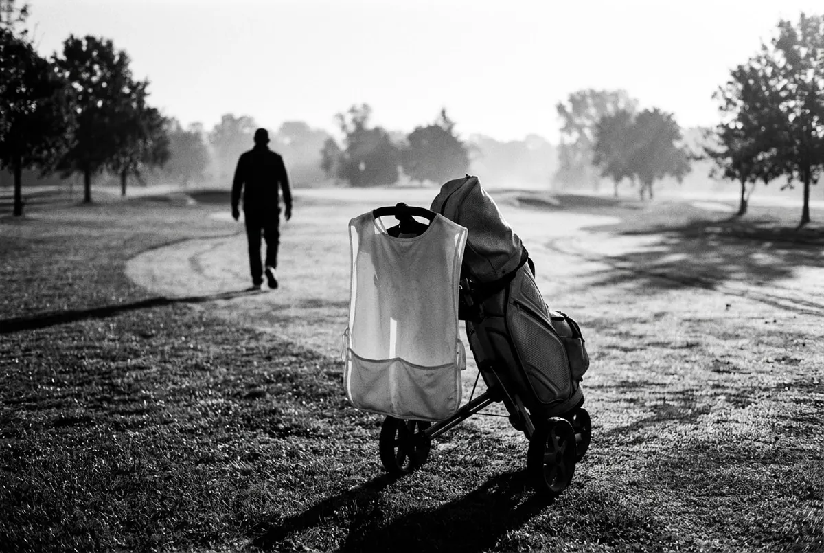 Silhouet van een caddie met golftas op de fairway bij ochtendlicht