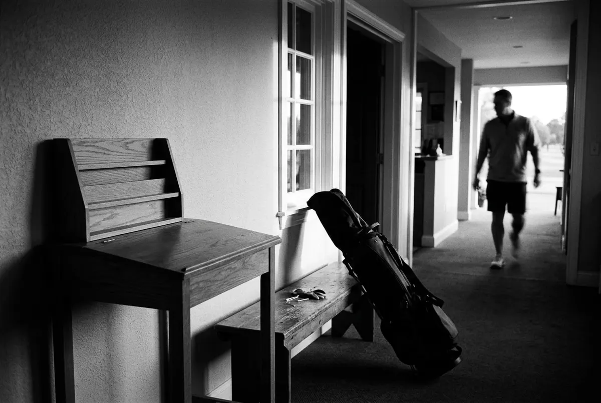 Lege inschrijfbalie bij een golfclub in de vroege ochtend, met een golftas tegen de bank