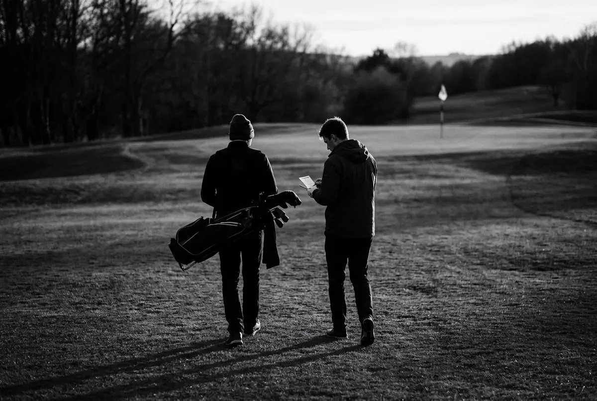 Twee golfers lopen over de fairway richting de green, op weg naar de afrekening bij de negende hole.