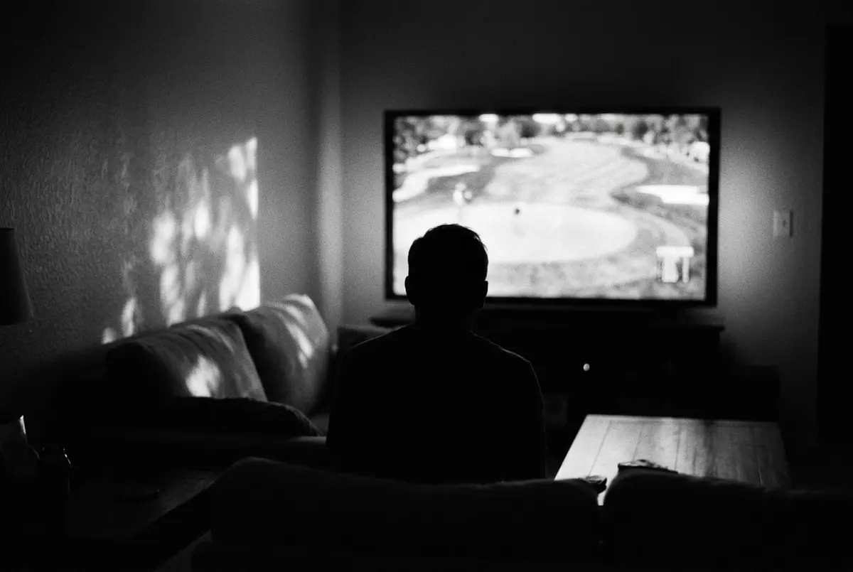 Silhouet voor een televisiescherm dat een golfbaan toont, in zwart-wit