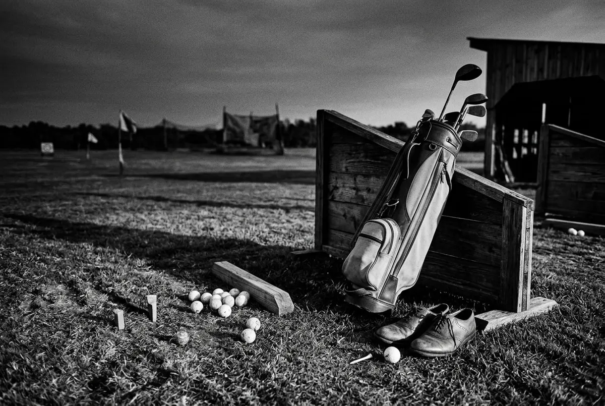 Vintage driving range in zwart-wit met verspreide golfballen en een club tegen een tas, sfeerbeeld bij het verhaal over Fred Astaire en golf.