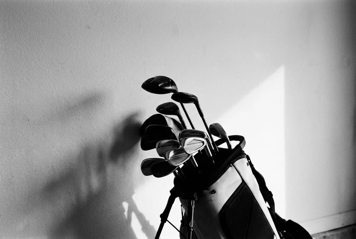 Minimalistische zwarte golftas met clubs tegen een lege muur, in zwart-wit.