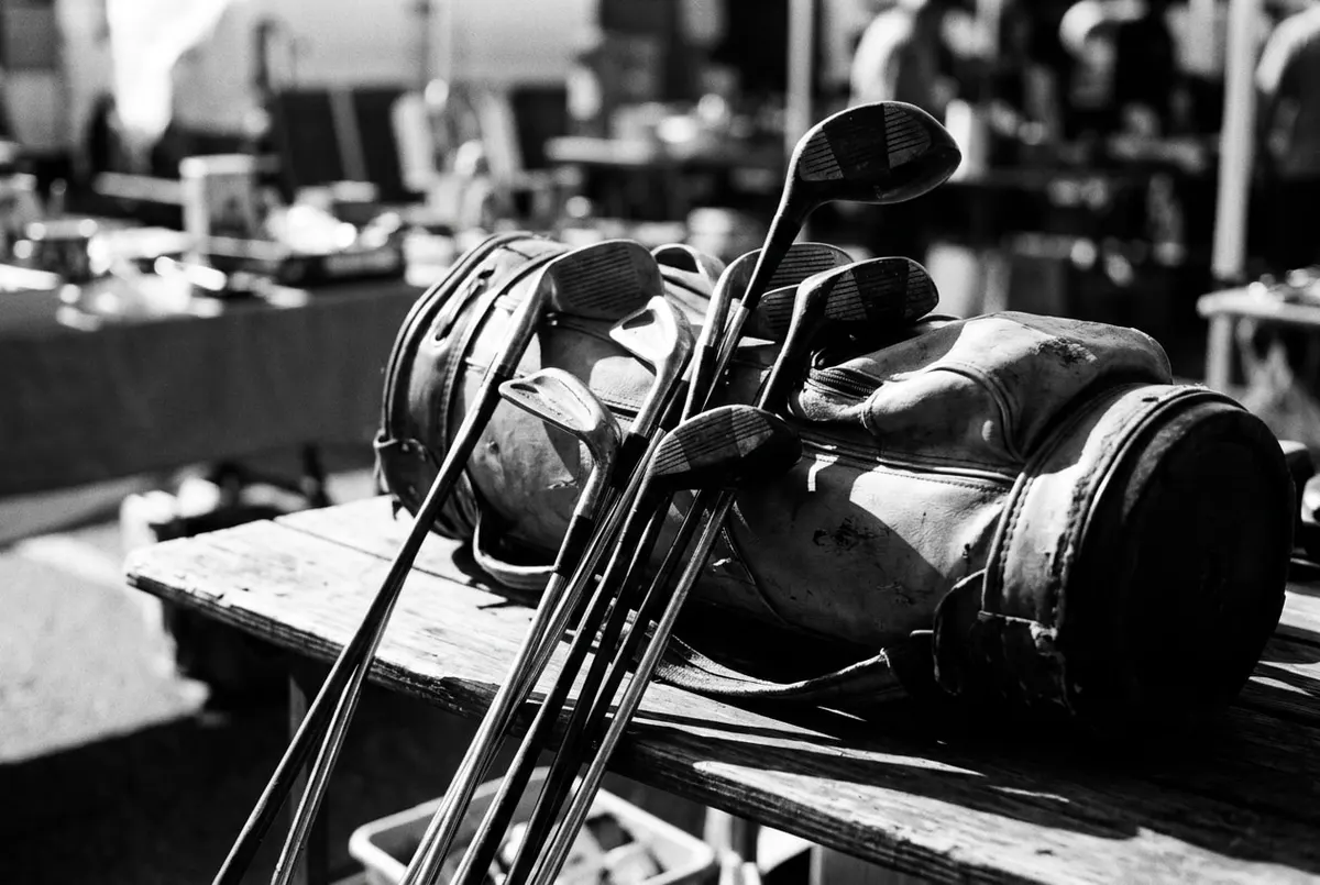 Tweedehands golfclubs uitgestald op een markttafel, in zwart-wit