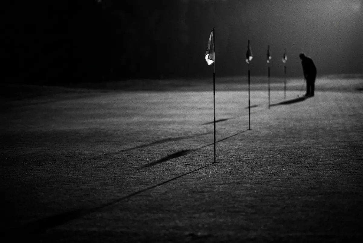 Rij vlaggenstokken op een fairway bij schemering, met een silhouet bij de verste hole