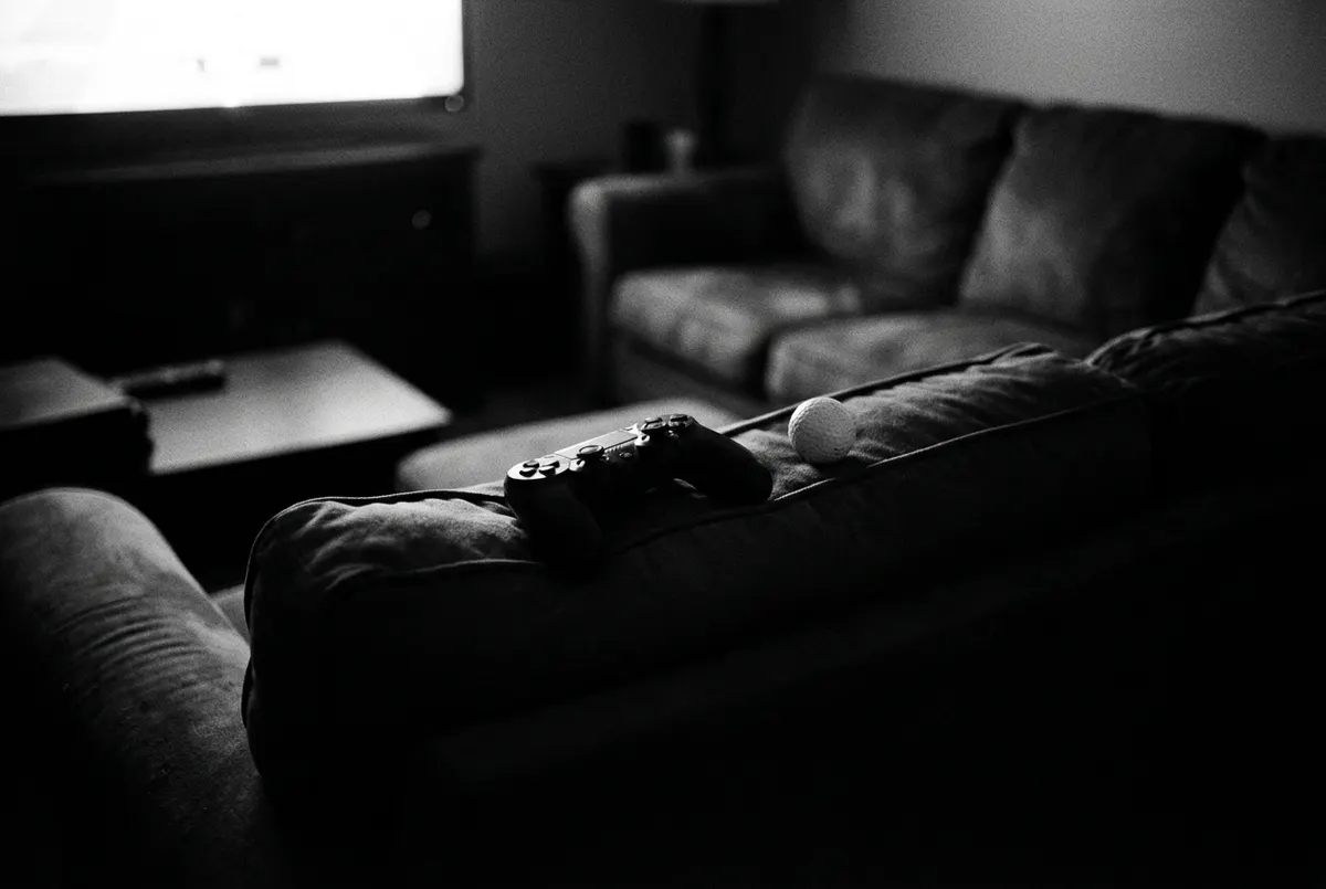 Een controller en een golfbal naast elkaar op een bank, verlicht door het schijnsel van een tv in een donkere kamer.