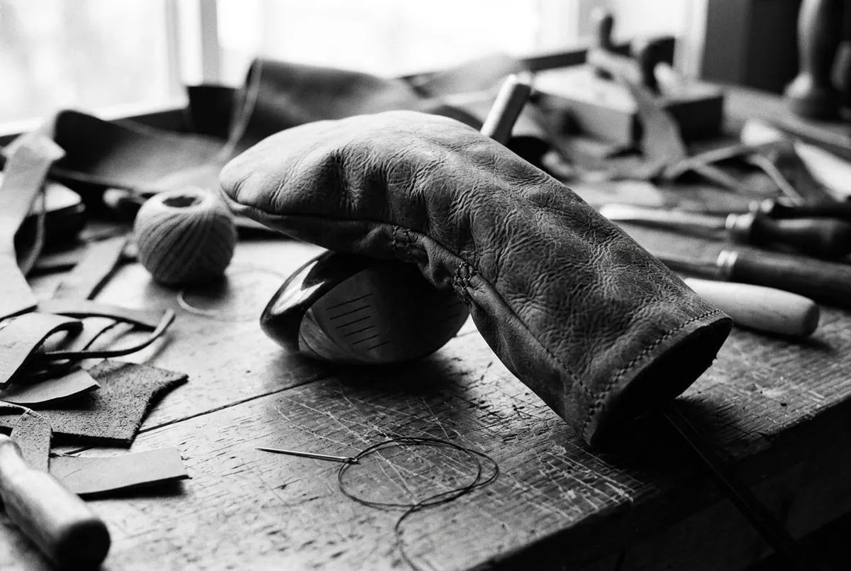 Handgemaakte leren headcover op een golfclub, met naaigaren en leerresten op een werkbank