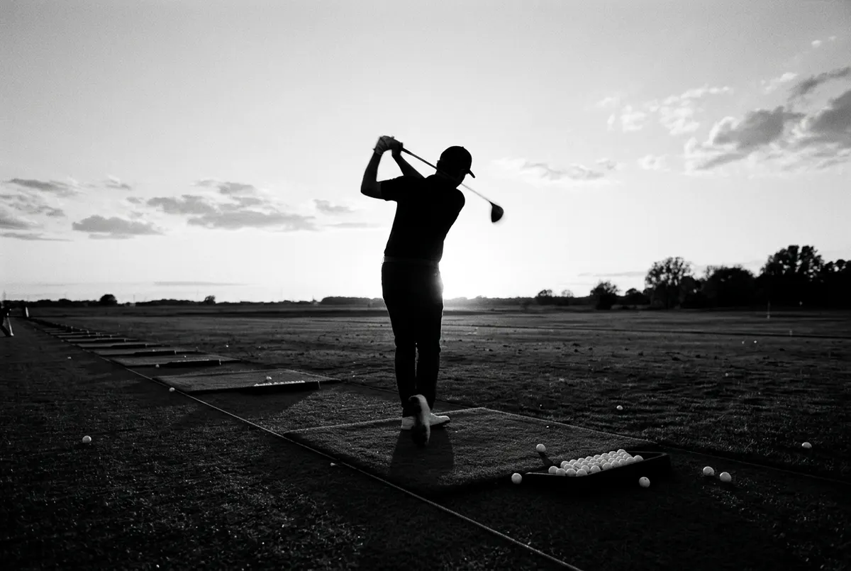 Silhouet van een golfer die oefent op een driving range bij avondlicht, zonder dat daar een golfvaardigheidsbewijs voor nodig is.