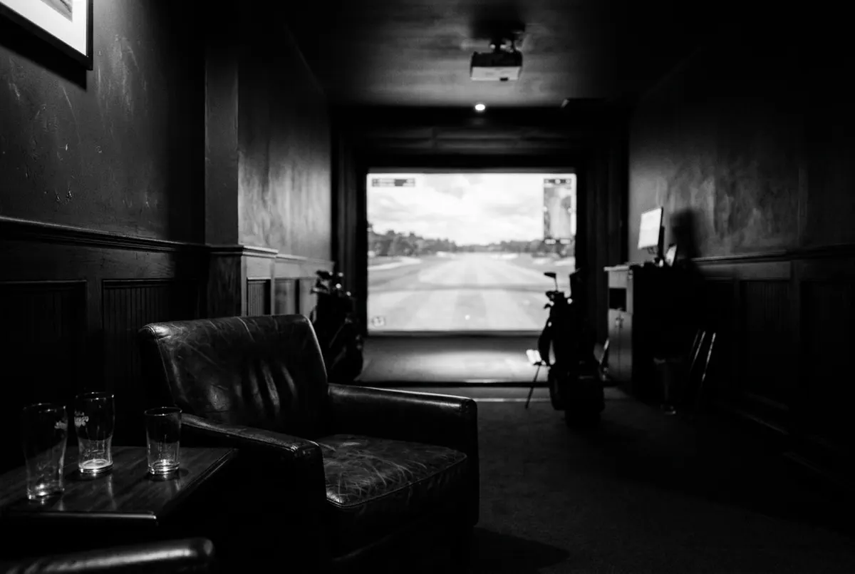 Donkergroene indoor golflounge met een verlicht simulatorscherm, geen mensen in beeld