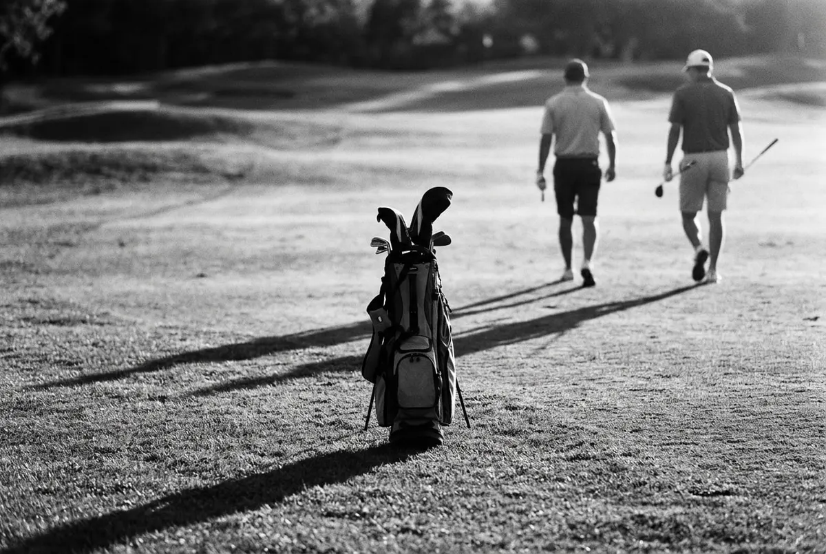 Golftas met een lege slot op de fairway, twee golfers lopen op de achtergrond weg met een extra club