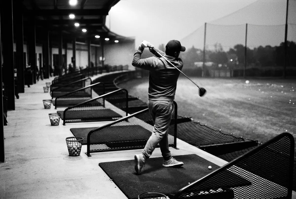 Golfer in silhouet slaat een bal op een driving range bij avondlicht