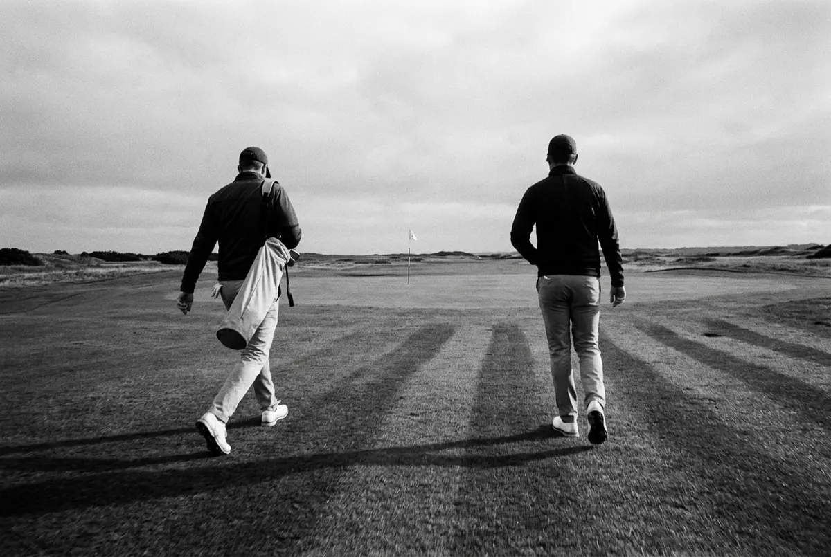 Twee golfers lopen in een hoog tempo over de fairway richting de green