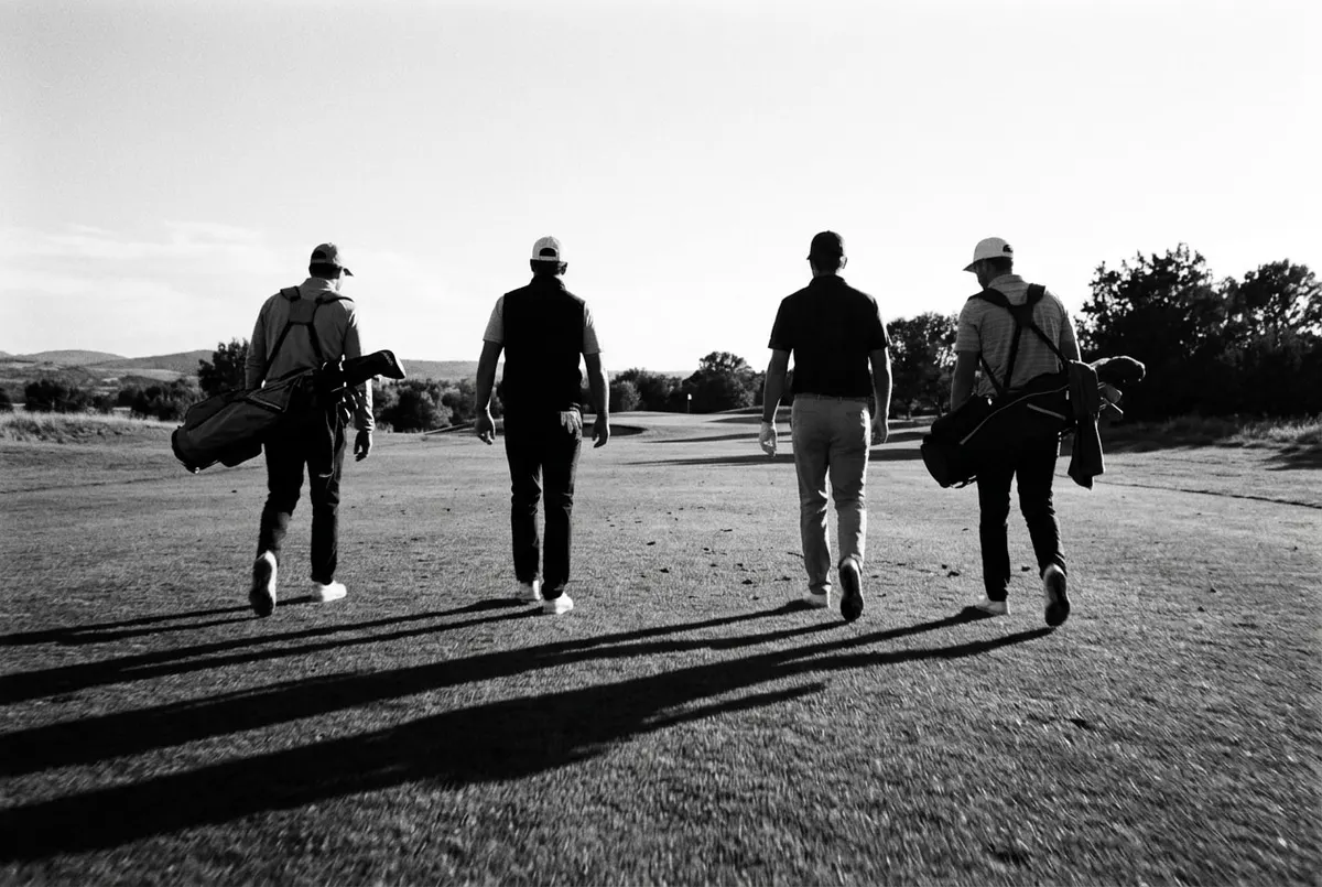 Vier golfers lopen in koppels over de fairway tijdens een rondje in de avondzon