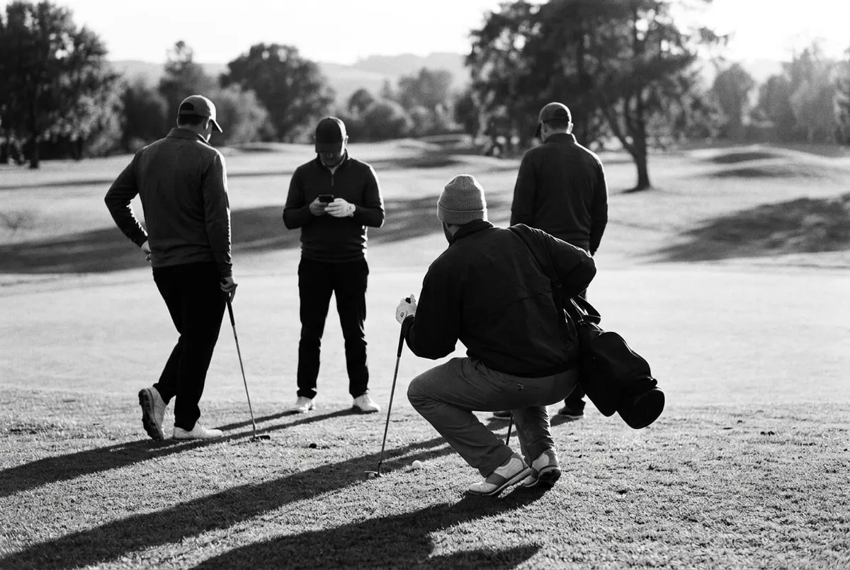 Vier golfers op de fairway, één speler bereidt zijn slag voor terwijl de anderen toekijken