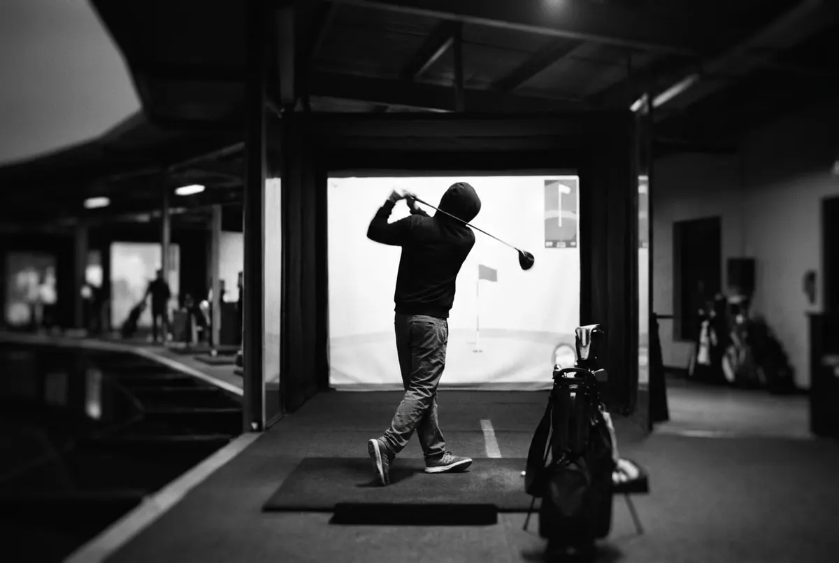 Golfer op een driving range slaat een bal richting een simulatorscherm tijdens het schemeren