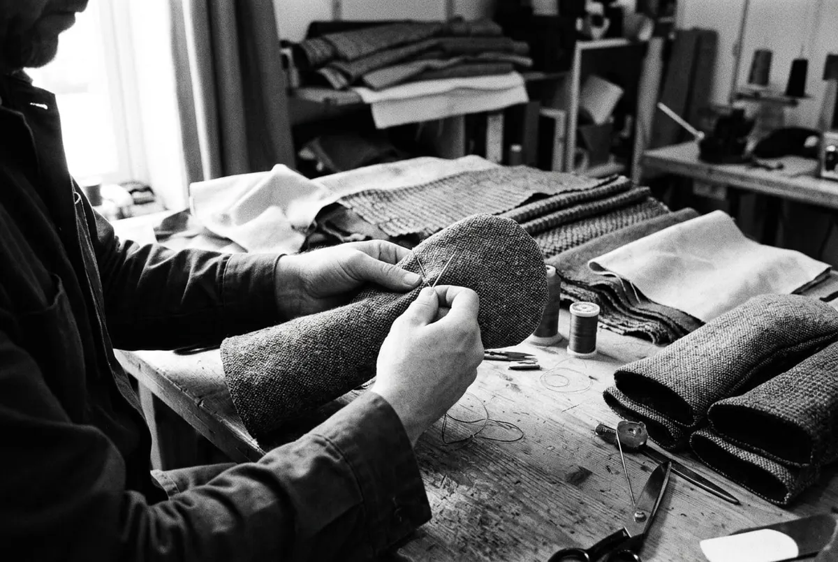 Handen werken aan een handgemaakte golf-headcover op een werkbank met stof, in zwart-wit