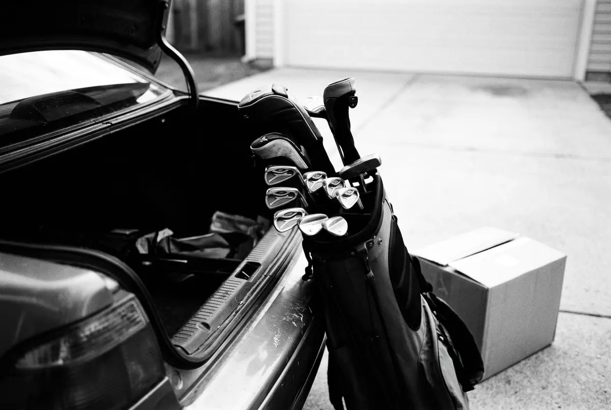Een complete golftas met clubs naast een kartonnen verzenddoos bij de kofferbak van een auto