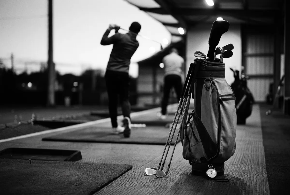 Golftas met uitgestalde clubs naast een stopwatch op een driving range in avondlicht