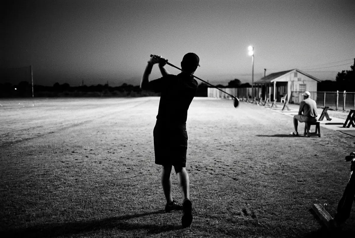 Golfer in silhouet slaat af op een driving range bij avondlicht, met een toeschouwer op de achtergrond