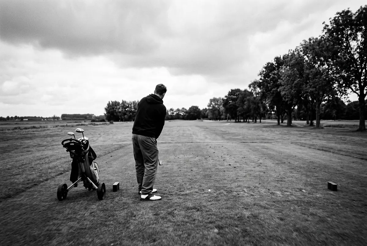Een golfer maakt zich klaar voor een afslag op een Nederlandse golfbaan onder een bewolkte lucht