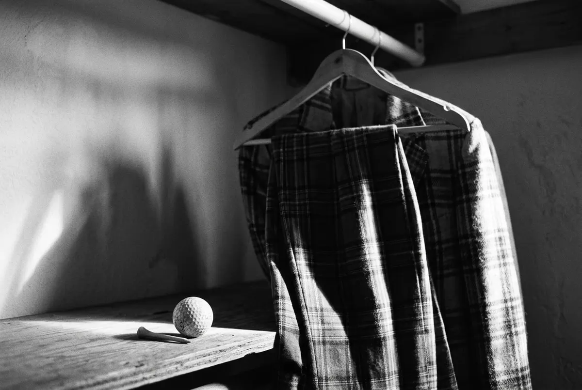 Vintage geruite golfjas en broek aan een kledingrek, in zwart-wit, met een golfbal en tee op de achtergrond.