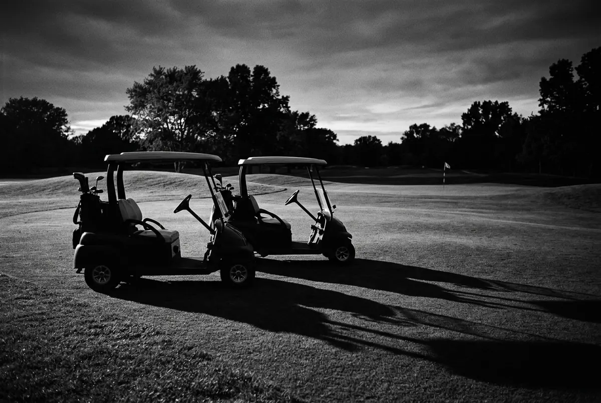 Twee lege golfkarretjes naast elkaar op een fairway bij avondlicht, symbool voor een rivaliteit op de golfbaan.