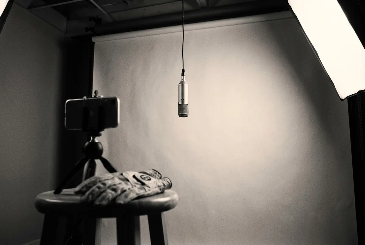 Een hangende microfoon in een lege studio, met een golfhandschoen en een telefoon op een tripod op de voorgrond.