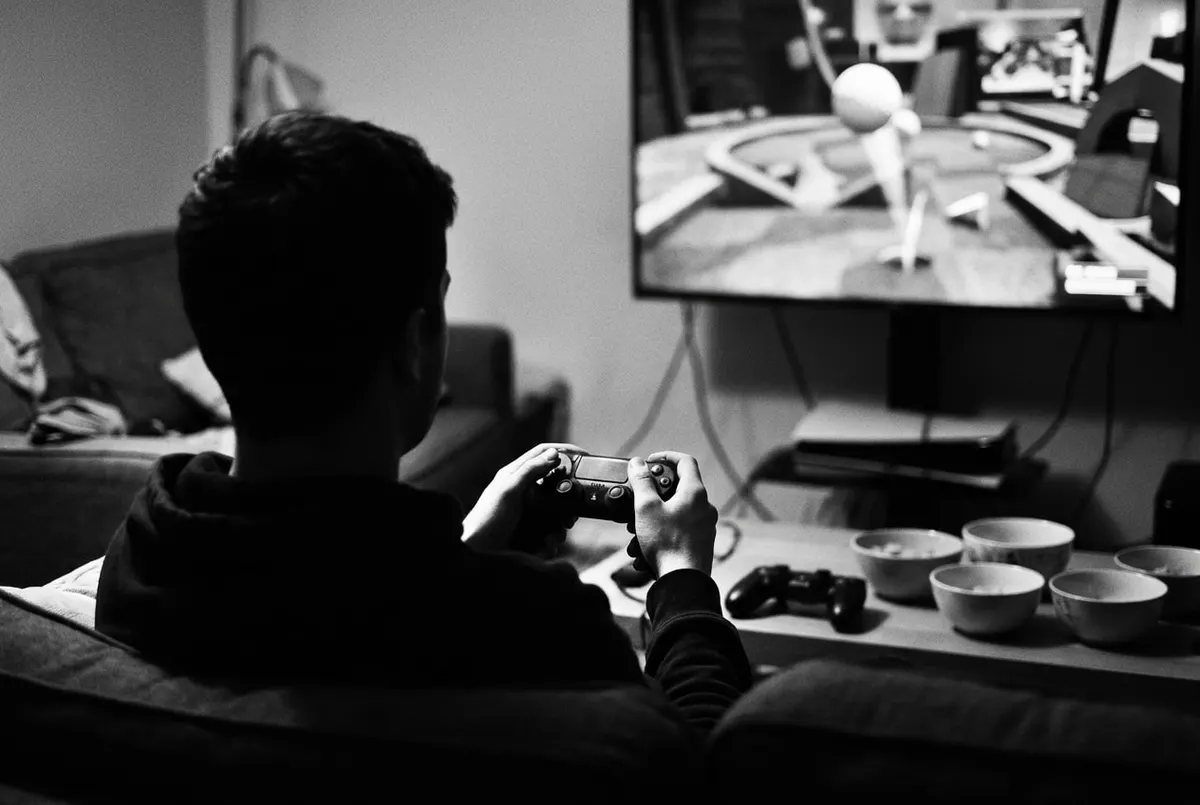 Silhouet van iemand met een controller voor een scherm met een chaotische minigolfbaan, in zwart-wit.