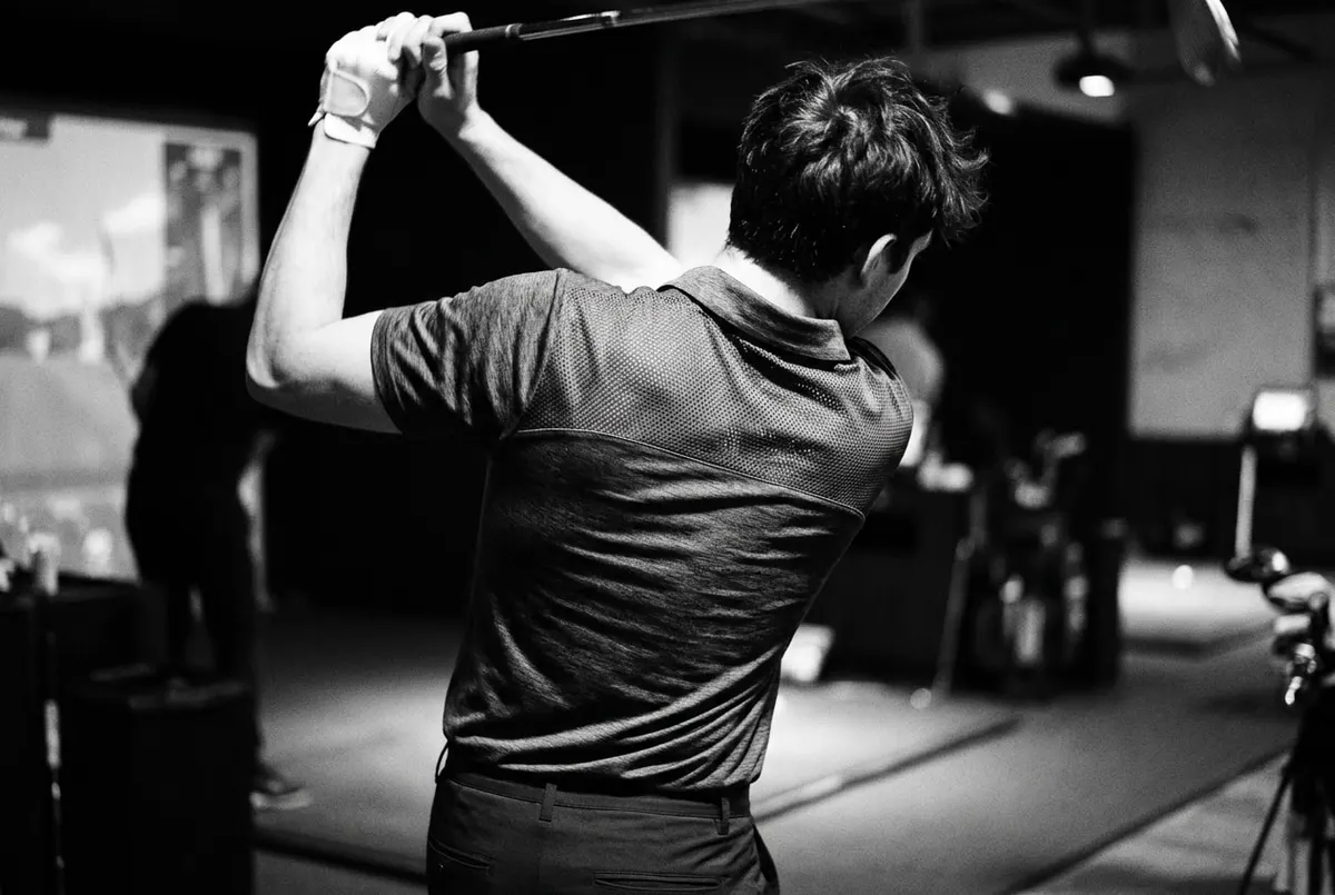 Close-up van de rug van een golfer in technische kleding met meshpaneel tijdens de swing op de driving range