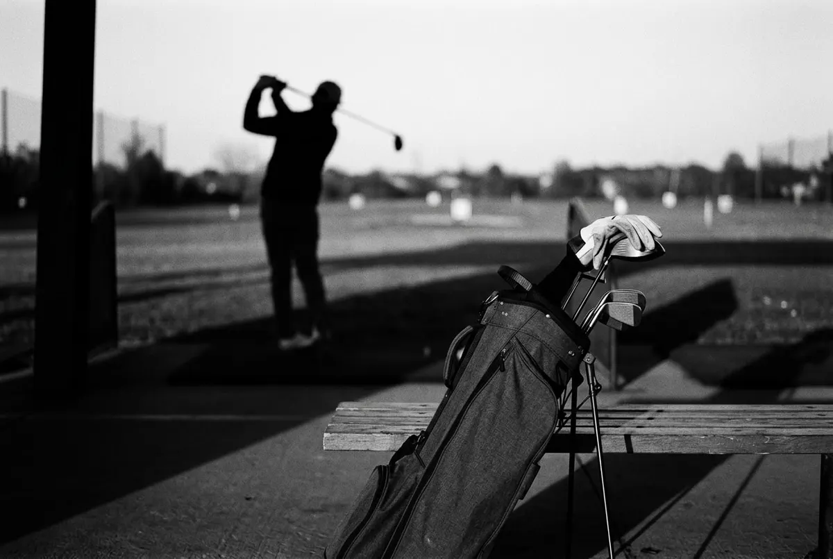 Silhouet van een golfer die oefent op een verlaten driving range in avondlicht, zwart-wit.