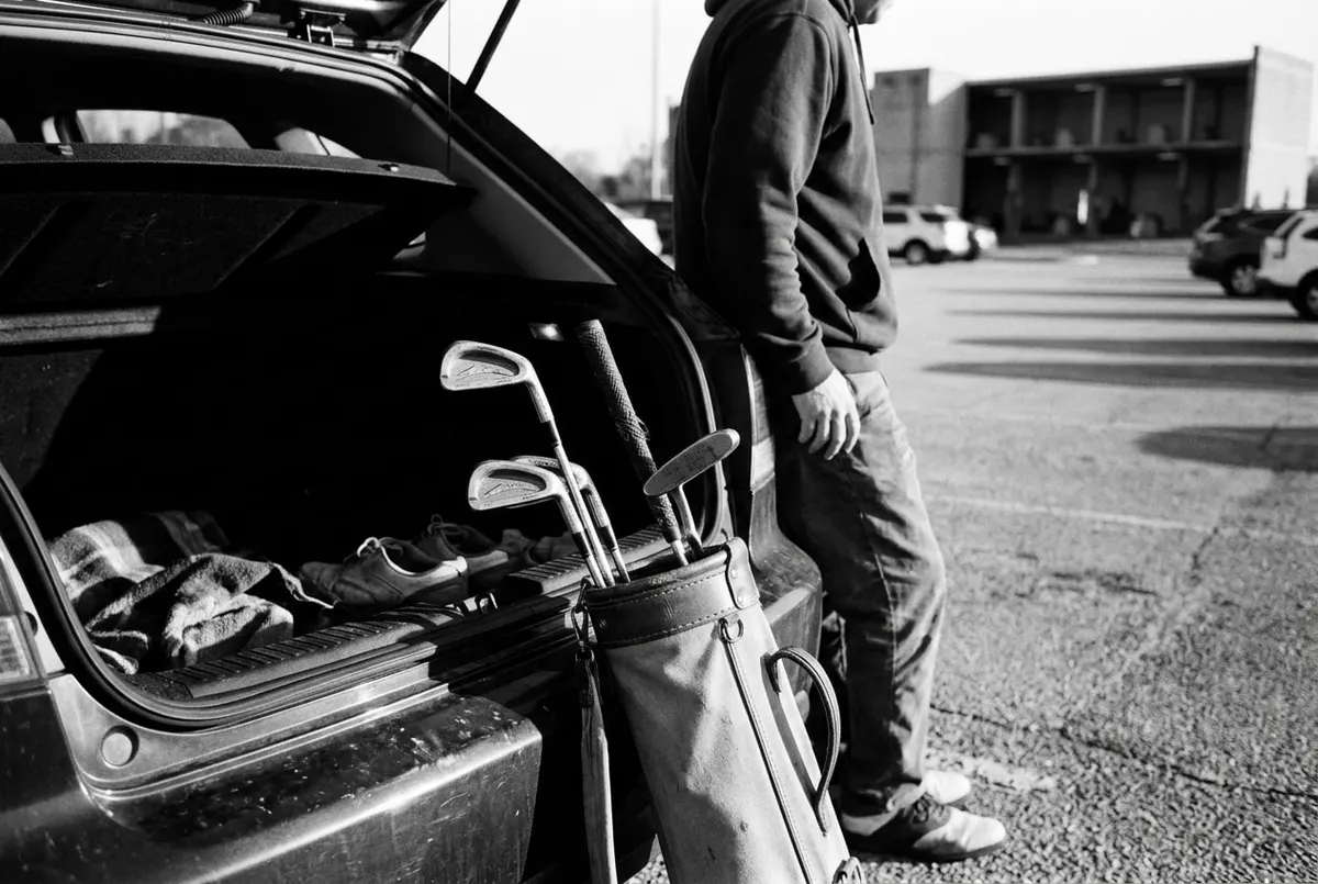 Een beperkte set golfclubs tegen de kofferbak van een auto op een parkeerplaats bij een driving range